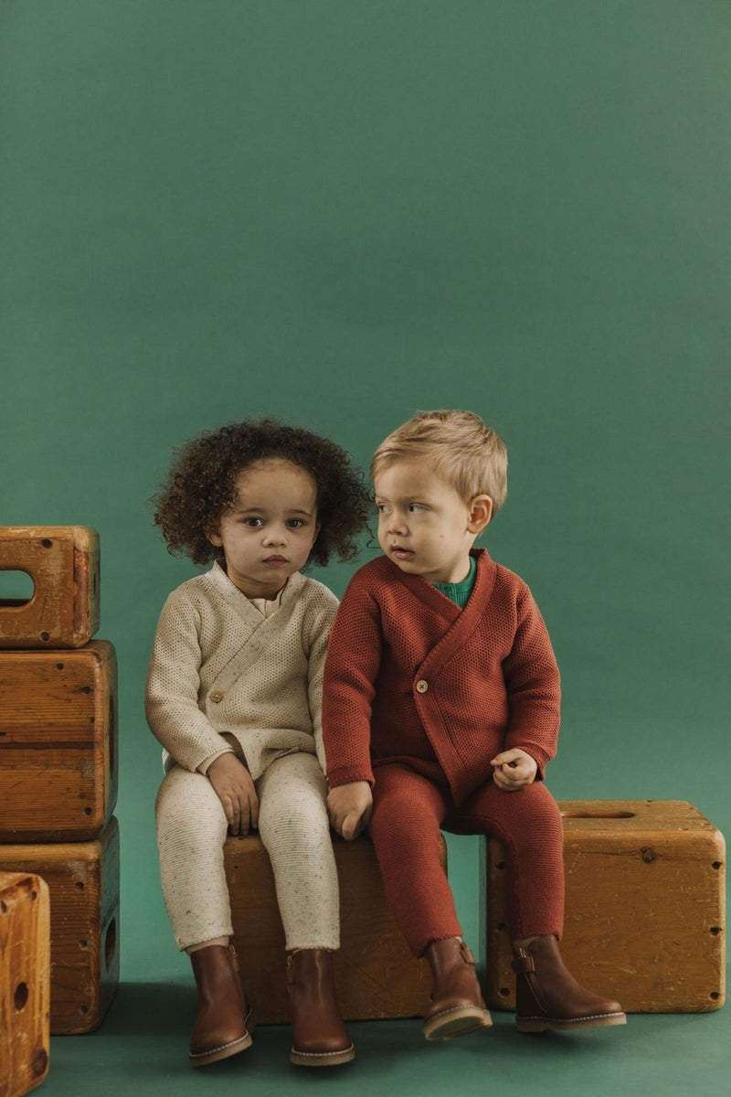 Fin & Vince chapter 2 - toddlers wearing knit suspender pants and wrap cardigans in gingerbread and confetti while sitting on vintage luggage