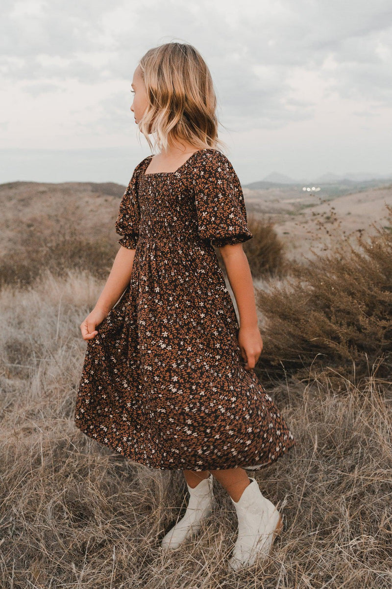 Rylee + Cru AW21 Drop 2 Lifestyle photo of a girl wearing the Adelaide dress in Winter Bloom, looking off in the distance at rolling hills while standing in a field during autumn. 